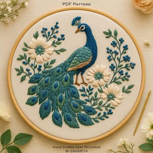May include: Embroidered peacock design in a wooden hoop. The peacock is rendered in shades of blue and green, with a detailed tail. Cream-colored flowers and blue berries surround the peacock. The text "PDF PATTERN" and "HAND EMBROIDERY PATTERNS BY ZAZARITA" are visible.