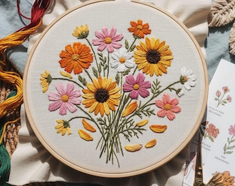 May include: A hand-embroidered floral design in a wooden hoop. The embroidery features a bouquet of colorful flowers, including orange, pink, yellow, and white daisies. The text "Hand Embroidery Patterns by Zazarita" is at the bottom.