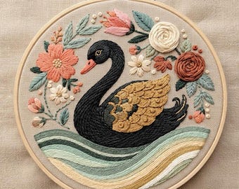 May include: A circular embroidery hoop containing a hand-stitched design of a black swan with gold-toned wings, surrounded by a floral wreath of pink, cream, and rust-colored flowers and green leaves, set against a light beige fabric background.