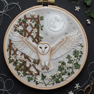 May include: Embroidered artwork in a hoop, depicting a barn owl with open wings under a moonlit sky. The design incorporates a wooden trellis, white flowers, and green leaves, all created with detailed thread work in various colours.