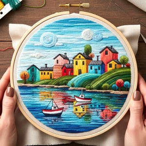 Puede incluir: Una colorida escena de paisaje bordada en un aro de madera. La obra de arte representa un pueblo frente al mar con casas de varios colores, un lago azul con dos barcos y un cielo azul con nubes esponjosas. El bordado está hecho con hilos de varios tonos.