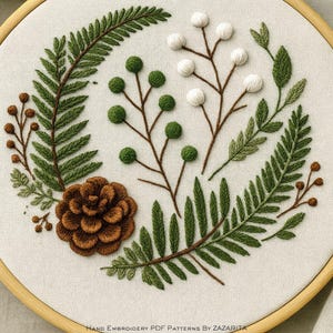 May include: An embroidered botanical design featuring a brown pinecone, green fern leaves, and branches with green and white spherical accents. The design is set on a cream-colored fabric and framed in a wooden hoop.