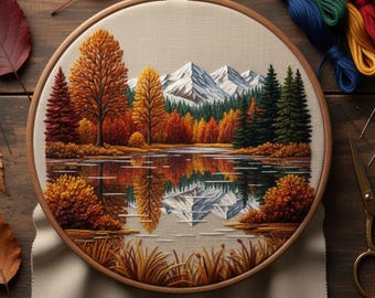 May include: A hand-embroidered landscape scene in a wooden hoop. The design features a lake reflecting colorful autumn trees and snow-capped mountains. The embroidery uses shades of orange, red, green, and blue. The text at the bottom reads "Hand Embroidery PDF Patterns By Zazarita."
