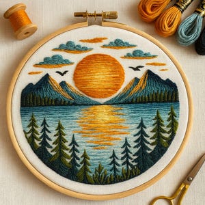 May include: Embroidered landscape art in a wooden hoop. The design features a sunset over a lake with mountains, trees, and birds. The colour palette includes shades of orange, blue, and green. Embroidery floss and a spool of thread are visible.