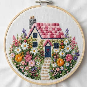 Puede incluir: Escena bordada de una casa en un aro de madera. La casa tiene un tejado a cuadros rosa y blanco, una puerta azul con un corazón y está rodeada de flores coloridas. El texto "HAND EMBROIDERY PDF PATTERNS BY ZAZARITA" está en la parte inferior.