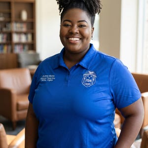 May include: A bright blue polo shirt featuring a white embroidered crest with the letters ZΦB on the left chest and white text on the right chest that reads Andrea Banks, Omicron Theta Zeta, Fairfax, Virginia, with a classic collar and buttons.