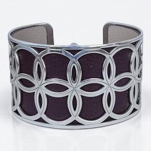 May include: Wide cuff bracelet with a silver-tone metal overlay featuring a repeating floral pattern. The interior is a deep purple color, and the inside band is a light gray. The bracelet has a modern, open design.