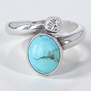 May include: A silver ring with a large oval turquoise stone. The ring has a distinctive design with a smaller, textured circular accent. The turquoise stone is a vibrant blue-green colour, set in a polished silver band.