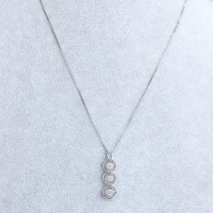 May include: A silver necklace with a pendant featuring three round, sparkling gemstones. The pendant has a delicate, intertwined design. The necklace is displayed against a light gray background.