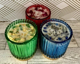 May include: Three glass candle jars with different colored glass and embedded crystals. The candles are white and the jars are red, green, and blue.