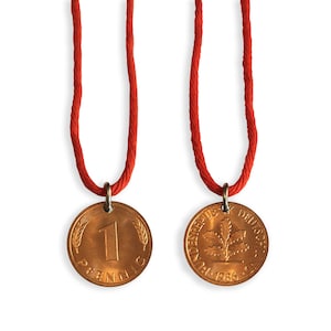 Peut inclure: Deux pendentifs en forme de pièces de monnaie cuivrées sur des cordons rouges. Une pièce porte le chiffre "1" et le mot "Pfennig". L'autre pièce montre un motif de feuille de chêne et les mots "Bundesrepublik Deutschland" et l'année "1986".