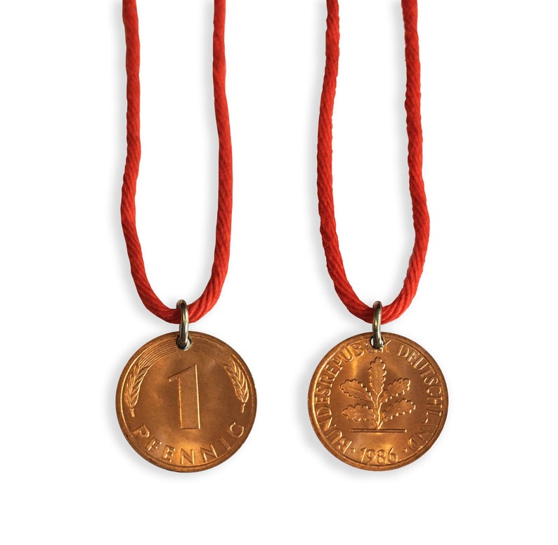 May include: Two copper-colored coin pendants on red cords. One coin shows the number "1" and the word "Pfennig". The other coin shows an oak leaf design and the words "Bundesrepublik Deutschland" and the year "1986".