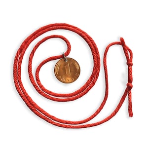 May include: A red cord necklace with a bronze coin pendant. The coin features the number "1" and the word "Pfennig". The cord is knotted at the end.