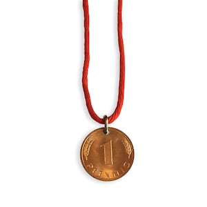 May include: A copper-colored pendant necklace featuring a vintage 1 Pfennig coin. The coin is suspended from a red cord necklace. The coin has the number 1 and the word "Pfennig" visible.