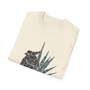 May include: A beige t-shirt with a black and blue graphic of a bull's head and a plant with sharp leaves.