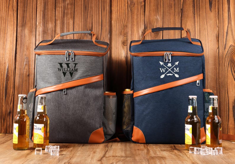 Pu&ograve; includere: Due zaini frigo isolanti, uno grigio e uno blu navy, con finiture in pelle marrone. Lo zaino grigio ha il nome "WILLIAM" stampato sopra. Lo zaino blu navy ha un emblema bianco. Entrambi hanno un manico e tasche laterali.