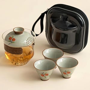 May include: A tea set featuring a glass infuser, three small cups, and a black carrying case. The infuser has a wooden band and a lid with a floral design. The cups and lid feature an orange and green floral pattern.