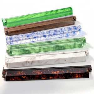 Puede incluir: Una colección de bandejas rectangulares decorativas en varios materiales y colores. Las bandejas incluyen acrílico verde, madera, acrílico transparente con diseños florales azules, mármol y patrones de carey. Cada bandeja tiene un diseño único.