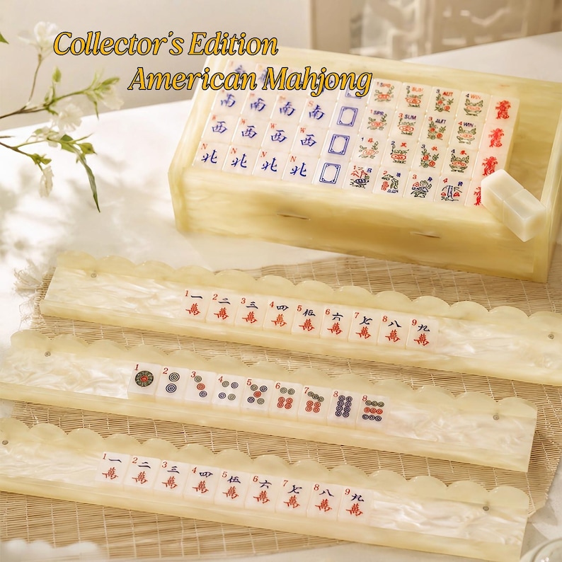May include: A Collector's Edition American Mahjong set featuring cream-colored, marbled resin tiles and matching racks. The set includes a storage box filled with tiles, and three racks displaying various numbered and patterned game tiles.