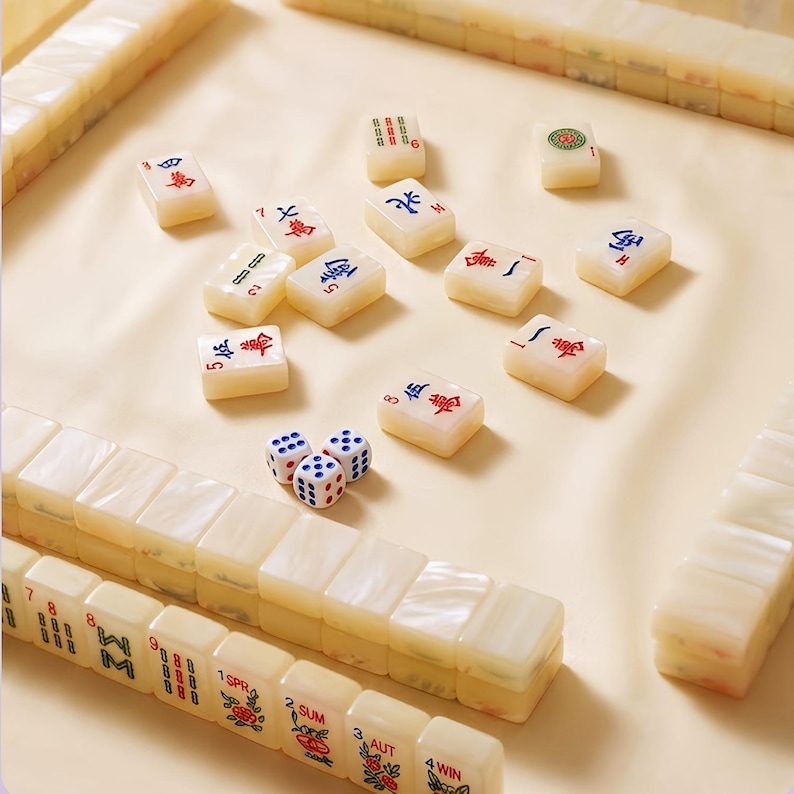 May include: A set of off-white Mahjong tiles with red, blue, and green engraved characters and symbols. The set includes several rows of stacked tiles, scattered individual tiles, and three small white dice with blue and red pips.
