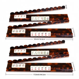 May include: Set of five brown and tan Mahjong tile racks. Each rack is 2.7 inches (7 cm) high and features a scalloped edge. The longest rack is 20 inches (50.8 cm) long, and the shortest is 17.5 inches (44.5 cm) long. The racks hold white tiles with red and green markings.