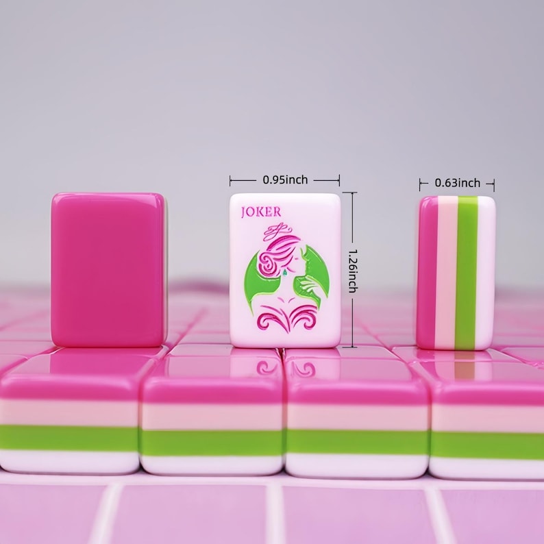 K&ouml;nnte beinhalten: Rosa und wei&szlig;e Mahjong-Steine mit gr&uuml;nen und rosa Akzenten. Ein Stein zeigt das Wort "JOKER" und eine Grafik einer Frau. Die Steine messen 2,4 cm breit, 3,2 cm hoch und 1,6 cm dick.