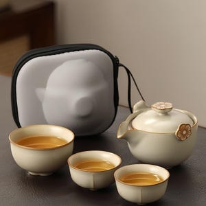 May include: A white ceramic tea set with a teapot, lid, and four cups. The set is in a black carrying case with a white interior.