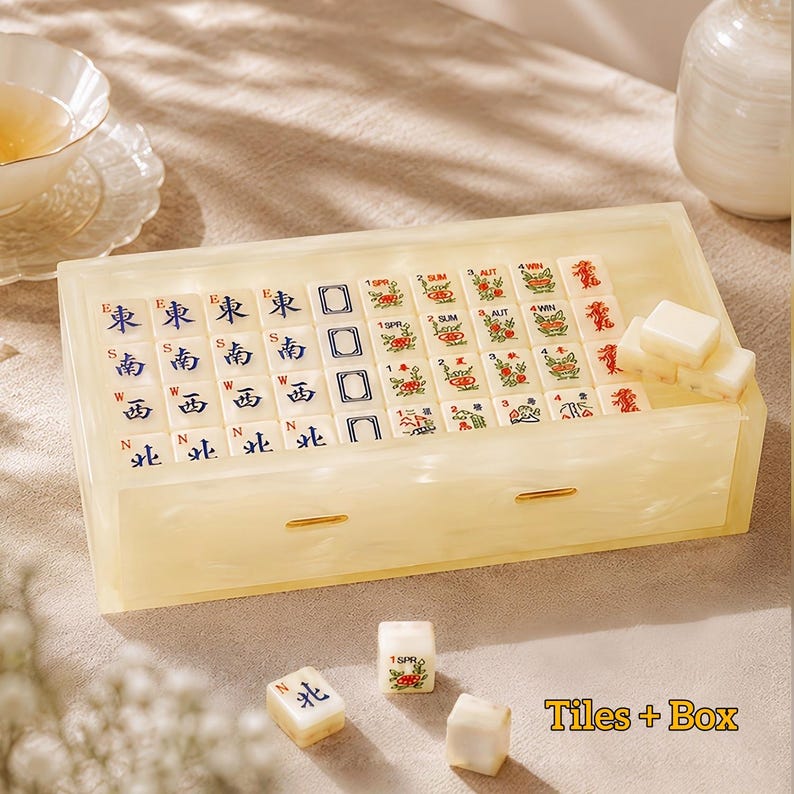 May include: A cream-colored, marbled resin box containing a set of Mahjong tiles. The tiles feature blue directional characters, green floral motifs, and red dragon symbols. Three loose tiles are placed in front of the box, and the text Tiles + Box is visible in the bottom right corner.