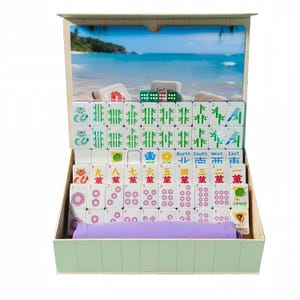 May include: A complete Mahjong set in a wooden box. The set includes white tiles with various symbols and numbers, green dice, and a purple tile holder. The box has a beach scene on the inside.