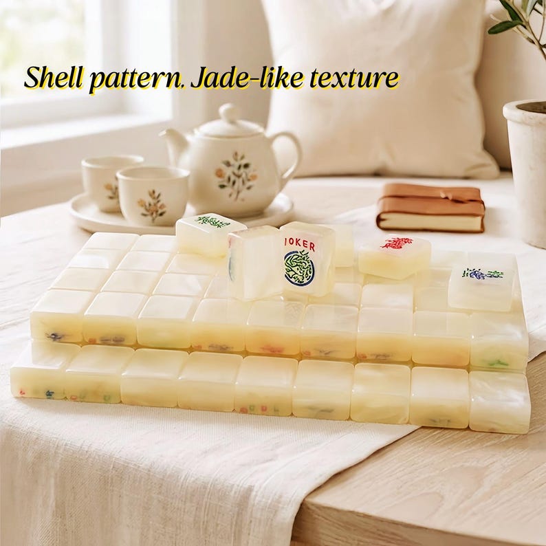 May include: A set of rectangular mahjong tiles with a cream-colored, jade-like texture and shell pattern. The tiles feature various engraved symbols and characters in red, green, and blue, including one tile clearly marked with the text JOKER.