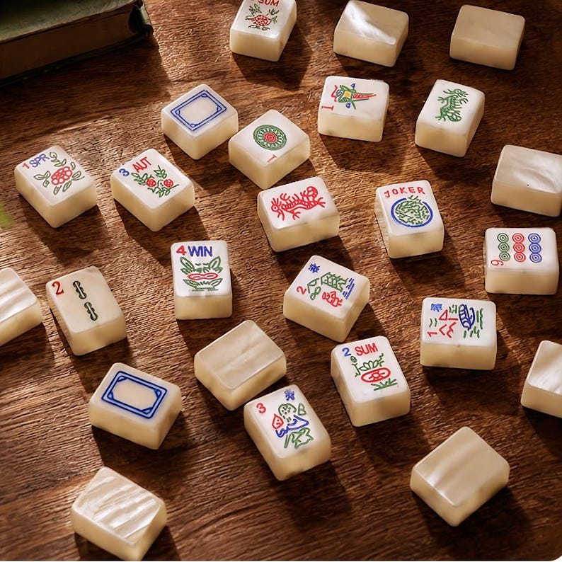 May include: A collection of off-white mahjong tiles scattered on a wooden surface. The tiles feature various colorful engraved designs, including floral patterns, numbers, and text such as 1 SPR, 3 AUT, 4 WIN, 2 SUM, and JOKER, with some tiles left blank.