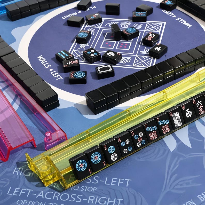 May include: A Mahjong set with black tiles and a blue playing surface. The tiles are arranged on the table, some in yellow and pink plastic holders. The tiles have various symbols and numbers. The game board has text that reads "WALLS LEFT" and "RIGHT".