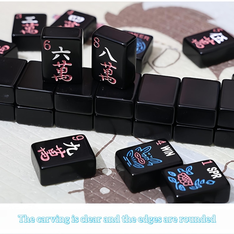 May include: Black Mahjong tiles with red and white Chinese characters and symbols. The tiles are arranged on a light-colored surface. The text "The carving is clear and the edges are rounded" is at the bottom.