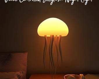 May include: A jellyfish-shaped night light with a glowing yellow dome and white tentacle-like strands. The text "Voice Controlled Jellyfish Night Light" is written above the lamp. White headphones rest on a wooden surface.