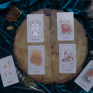 Op de afbeelding: Een spreiding van tarotkaarten op een houten oppervlak met een turquoise fluwelen achtergrond. De kaarten omvatten "Temperance", "The Lovers", "The White Wolf", "5 of Leaders", "Ace of Watchers" en "5 of Caretakers".