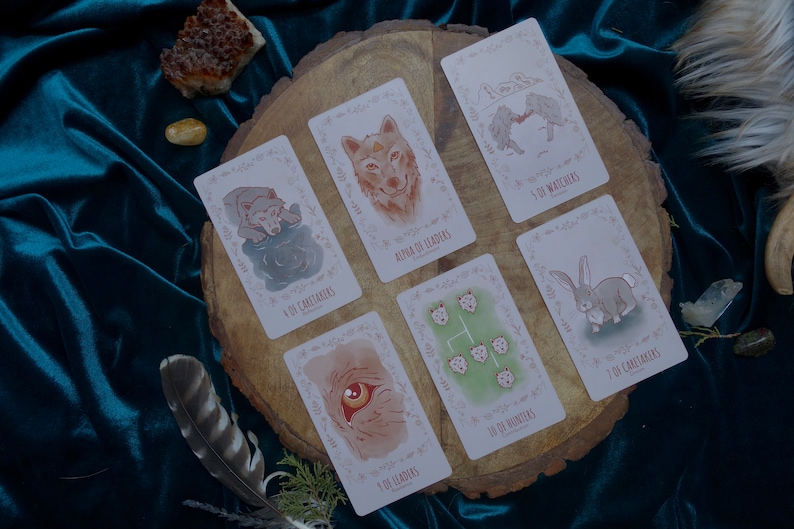 Op de afbeelding: Een set tarotkaarten met illustraties van dieren, waaronder een wolf, een konijn en een beer. De kaarten liggen op een houten oppervlak met een groene achtergrond.