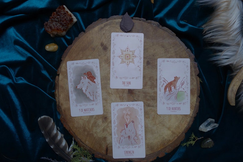 Op de afbeelding: Vier tarotkaarten op een houten oppervlak. De kaarten zijn uit het Wild Unknown Animal Spirit Deck. De kaarten zijn: 9 of Watchers, The Sun, 9 of Hunters, en Strength.
