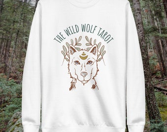 Op de afbeelding: Witte trui met een wolfillustratie en de tekst "THE WILD WOLF TAROT" in bruine letters.