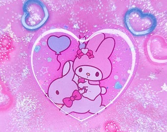 May include: A pink heart-shaped resin charm featuring a pink bunny holding a purple balloon, with a smaller pink bunny riding on its back. The charm is filled with glitter and iridescent flakes.
