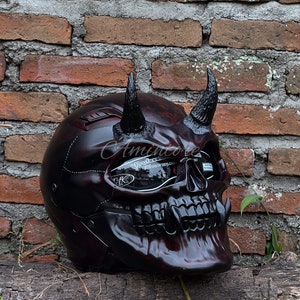 K&ouml;nnte beinhalten: Ein schwarzer und roter Motorradhelm mit Totenkopf-Design und H&ouml;rnern. Der Helm hat ein klares Visier mit dem aufgedruckten Text "Professional Visor Deploys".