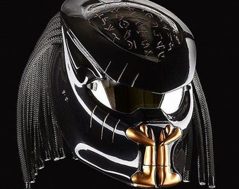 May include: A black motorcycle helmet with a gold-colored face mask and a black braided strap. The helmet has a glossy finish and features a design of symbols on the top.