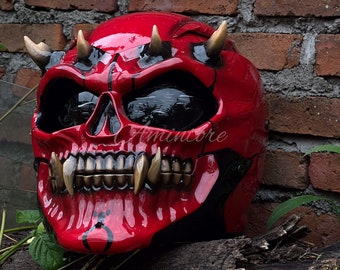 Könnte beinhalten: Roter und schwarzer Motorradhelm mit Totenkopf-Design und Hörnern. Der Helm hat ein schwarzes Visier und eine rote und schwarze Lackierung.