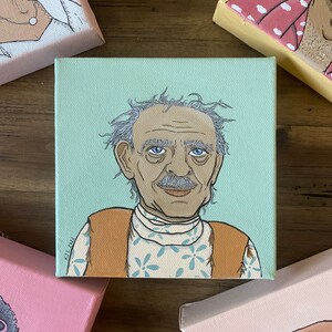 May include: A square canvas painting featuring a portrait of an elderly man with gray hair and a mustache. He wears a white shirt with a blue floral pattern and a brown vest. The background is light blue. Other paintings are visible.