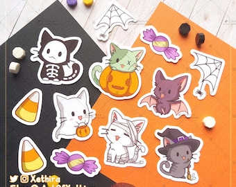 May include: A set of nine Halloween-themed stickers featuring cute cartoon cats in various costumes, including a skeleton, a mummy, a vampire bat, a witch, and a cat in a pumpkin. The stickers also include candy corn and a spider web.