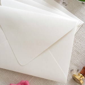 May include: A stack of white envelopes on a textured beige surface with pink flowers and a gold wax seal.