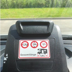 May include: A black dashboard display with a white sticker showing the dimensions of a vehicle. The sticker reads "Gesamtl&auml;nge 7,47m" and includes three red circles with the text "2,34m", "2,94m", and "3,5 t".