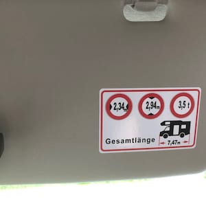 May include: A white sticker with red circles and black text. The circles show the maximum height, width, and weight allowed for a vehicle. The text says "Gesamtl&auml;nge 7,47m".