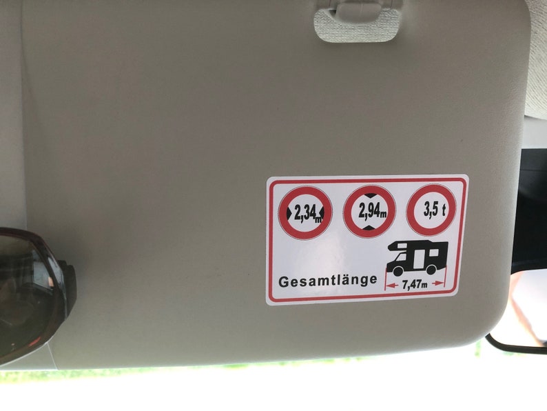 May include: A white sticker with red circles and black text. The circles show the maximum height, width, and weight allowed for a vehicle. The text says "Gesamtl&auml;nge 7,47m".