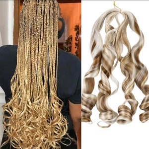 May include: A set of three blonde curly hair extensions with brown and white highlights. The extensions are tied together with a gold elastic band.
