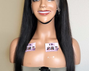 May include: A mannequin head displaying a long, straight black wig. The wig features a lace front and appears to be made of human hair. The mannequin is mounted on a black stand, set against a plain wall.